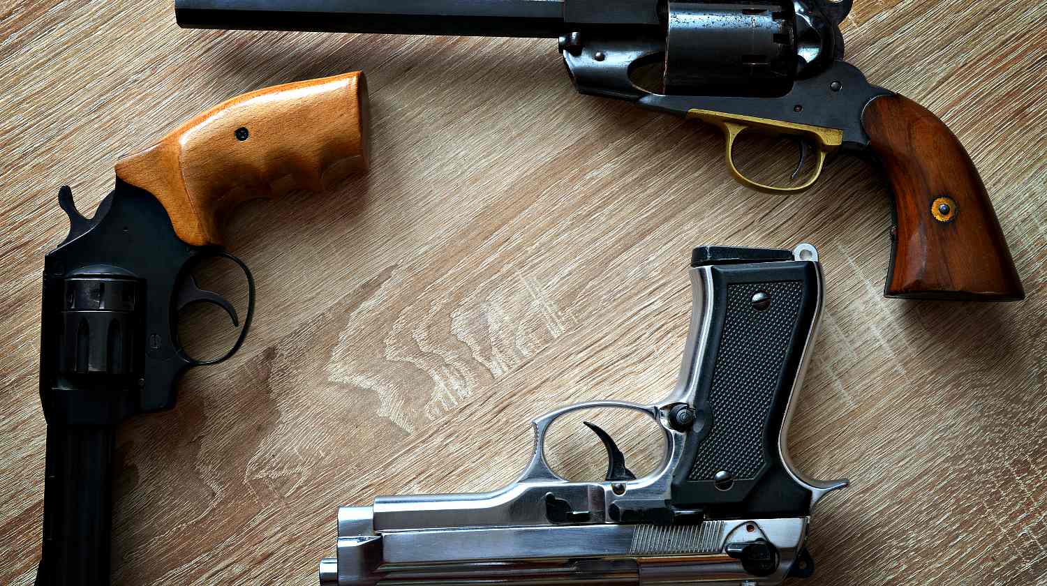 Three pistols on wooden board | Revolvers for Survival | The Best Guns That Stood The Test Of Time | Featured