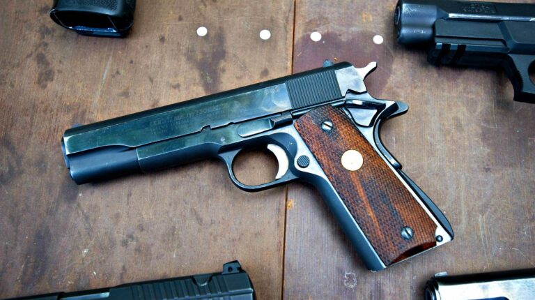 Feature | Black pistols on a wooden table | Colt Defender Series | Gun Carrier Compact Pistol Review