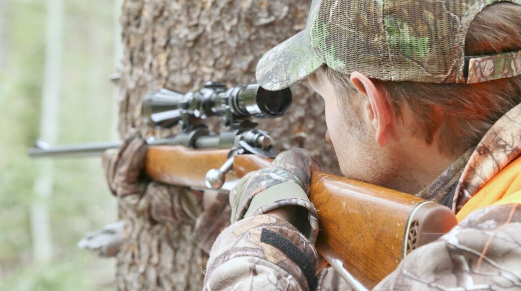 hunter soldier behind tree aiming his rifle at a target | The American Sniper Rifles: Rifles Used by American Sniper Chris Kyle | american sniper rifles | m24 sniper rifle | Featured
