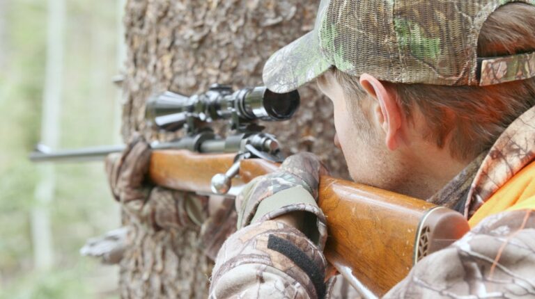 hunter soldier behind tree aiming his rifle at a target | The American Sniper Rifles: Rifles Used by American Sniper Chris Kyle | american sniper rifles | m24 sniper rifle | Featured